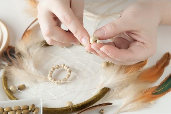 kvinde laver drømmerfanger med perler og fjer